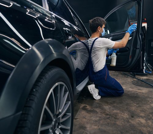 Man in repair workshop washing car window during car valeting